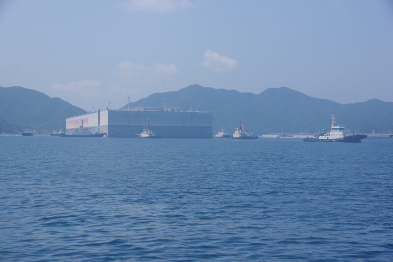 無数のタグボートに囲まれた巨大な物体が長崎港に入港